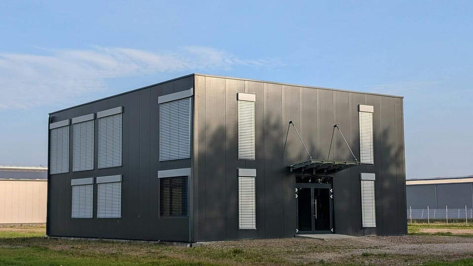 Modern industrial building with a sleek black exterior, photographed against a clear sky.